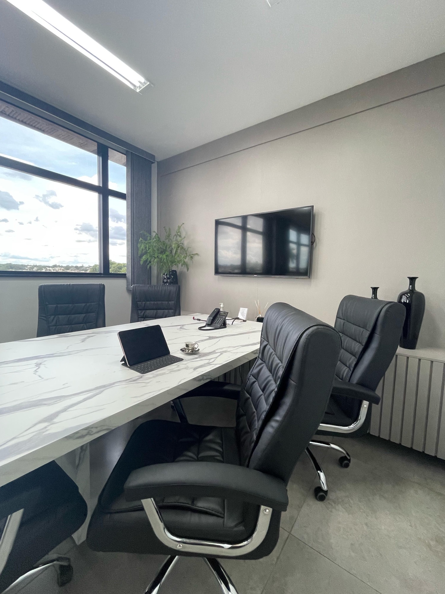 Sala de reunião do B.office, com mesa de mármore, cadeiras de couro e TV de parede.